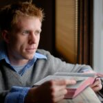 man in blue sweater reading book