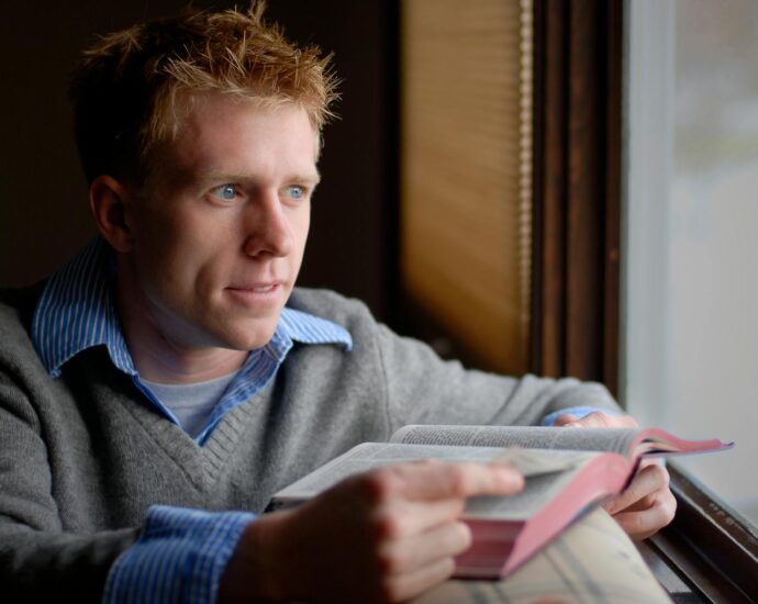 man in blue sweater reading book
