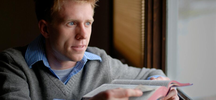 man in blue sweater reading book