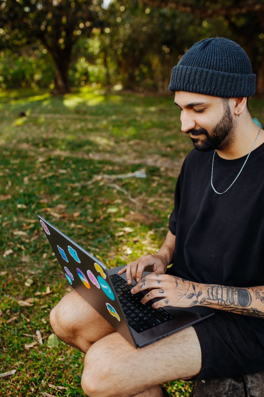 smiling man sitting with laptop against trees