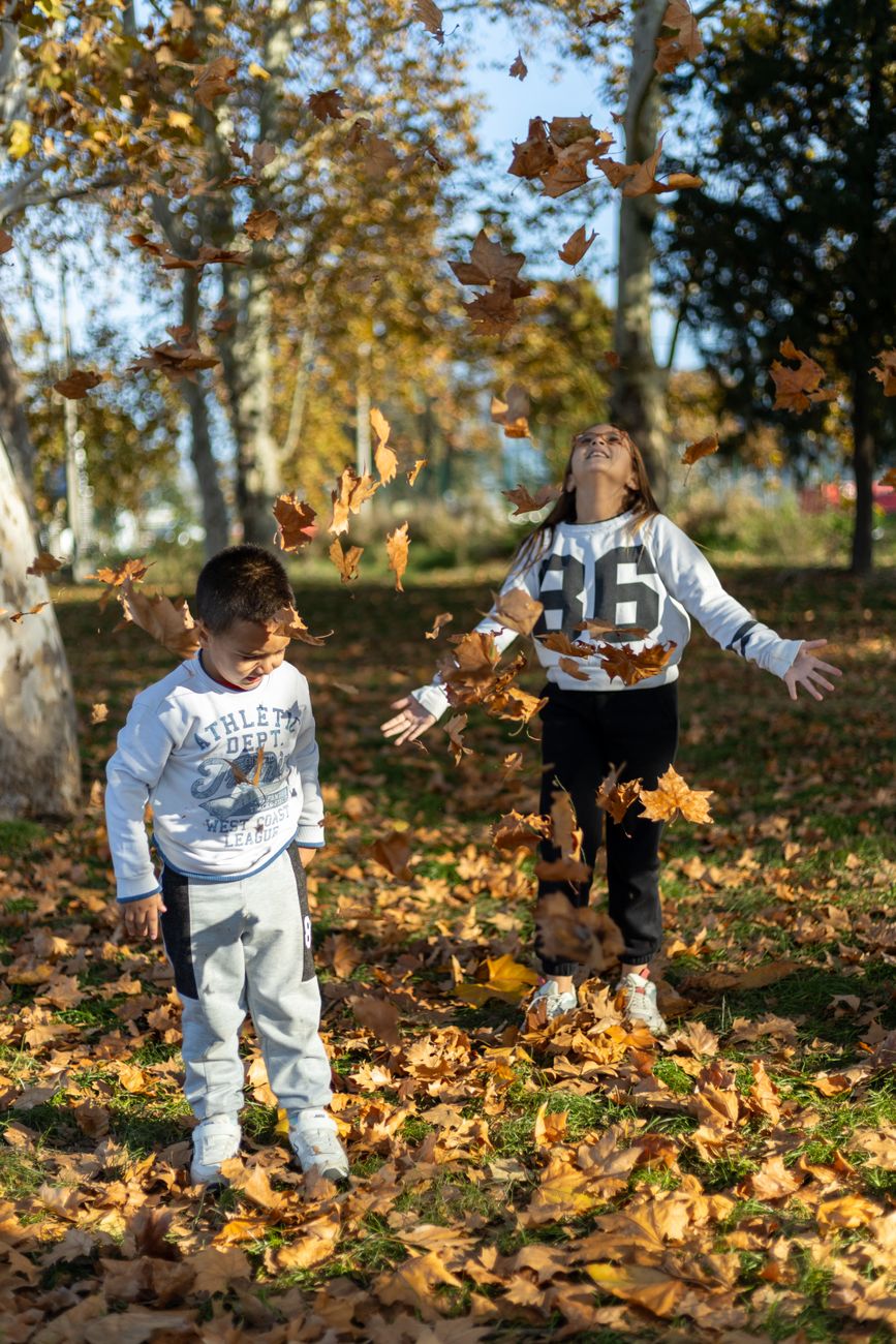 children playing with autumn leaves in park